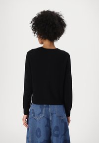 Svart strikket genser med lange ermer, rund hals og en litt cropped passform, kombinert med et blått denimskjørt med blomsterpriser.