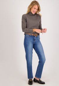 Grijze coltrui met lange mouwen, blauwe rechte jeans en zwarte instappers met gouden accenten. Eenvoudig en klassiek ontwerp.