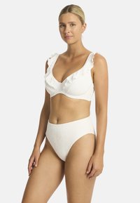 Weißes Bikini-Set mit strukturiertem, gemustertem Stoff. Der Oberteil hat Rüschenträger und einen tiefen Ausschnitt; der hoch geschnittene Unterteil hat eine glatte Oberfläche.