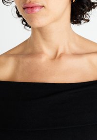 Fekete, váll nélküli felső, puha anyagból készült, testhezálló kialakítással, sima textúrával és széles nyakkivágással, amely kiemeli a kulcscsontot.