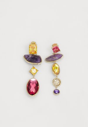 Boucles d'oreilles asymétriques avec monture en or et pierres précieuses facettées violettes, jaunes et roses, dont une avec un pendentif circulaire portant le logo de la marque.