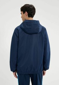 Dunkelblaues, leichtes Jackett mit Kapuze, elastischem Saum und glatter Textur; entworfen für den Freizeitlook und geeignet für verschiedene Wetterbedingungen.