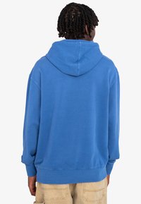 Sudadera azul de tejido suave, con un bolsillo tipo canguro, puños y dobladillo acanalados, y una capucha de longitud media en la parte posterior.