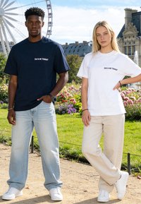 Deux adultes debout dans un jardin portant des jeans décontractés, des baskets blanches et des t-shirts avec l'inscription « TOI & MOI CE SOIR », avec une grande roue en arrière-plan.