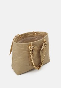 Sac à main matelassé beige avec des poignées en chaîne dorée tissées avec du tissu, comportant des anneaux dorés et un petit nœud en tissu de chaque côté.