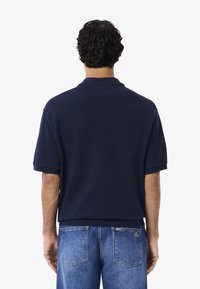 Mörkblå kortärmad polo med klassisk krage, i bomullsmaterial och med sidslitsar, kombinerad med ljusblå jeans.