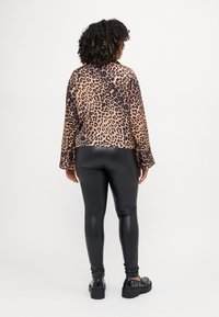 Blusa de estampado de leopardo com mangas longas, combinada com leggings pretas em pele sintética e sapatos de plataforma com detalhes de tachas.