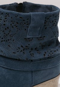 Ciemnoniebieskie zamszowe botki za kostkę z perforowanym kwiatowym wzorem na cholewce oraz płaską, teksturowaną podeszwą. Zawierają prosty element metalowy.