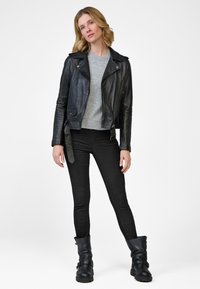 Schwarze Leder-Motorradjacke mit silbernen Reißverschlüssen, darunter ein grauer Pullover, schwarze Skinny-Jeans und schwarze knielange Stiefel. Einfaches Design.
