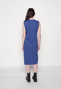 Vestido de jersey azul sem mangas com um corte ligeiramente relaxado, alcançando a altura da metade da panturrilha; os detalhes nas costas incluem um decote arredondado e aberturas laterais.