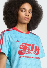 T-shirt azul claro com detalhes vermelhos, apresentando um grande gráfico e logotipo "Fly", mangas curtas e um padrão texturizado sutil.