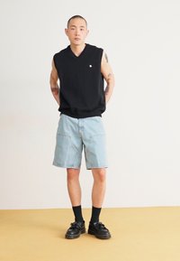 Black sleeveless sweater with a v-neck, light blue denim shorts, black shoes, and black socks. Simple, casual style with minimal detailing.