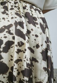 Flydende nederdel lavet af letvægtsstof med en cremefarvet bund og et brunprikket mønster. Har plisseringer og en elastisk talje.