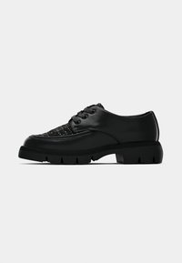 Chaussures noires en cuir avec un dessus tissé texturé, un design à lacets, une semelle en caoutchouc épaisse et une construction robuste.
