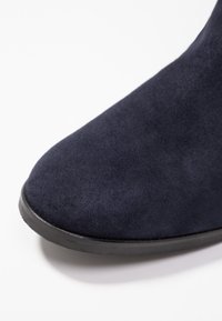 Bottine en daim bleu marine avec un bout arrondi et une surface lisse. Dispose d'une semelle en caoutchouc noire pour la durabilité. Aucun élément métallique ou accent visible.