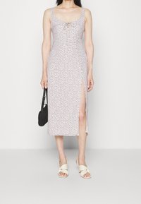 Blomstret midi-kjole med rund halsudskæring, knyt-frontdetalje, sideslids og let stof. Har bløde pink og blå mønstre. Båret med beige sandaler.