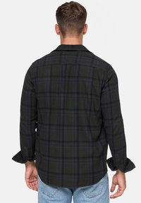 Camisa de cuadros en negro y verde con mangas largas, puños de botón y cuello. Ajuste entallado con una textura suave y detalle en el yugo trasero.