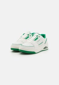 Fehér sneaker zöld részletekkel, sima bőrből készült felsőrésszel, perforált orral, párnázott nyelvvel és levegő párnázással a talpban.