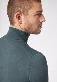 Dunkelblauer Rollkragenpullover mit strukturiertem Rippkragen und schmaler Passform, der nahtlose Schulterdetails und eine glatte Oberfläche zeigt.