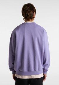 Sudadera lila, diseño de cuello redondo, mangas largas, puños y dobladillo acanalados. Material de algodón suave, corte holgado, llevada sobre una camiseta rosa clara.