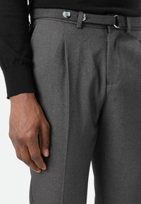 Graue, maßgeschneiderte Hose mit strukturiertem Stoff, doppelter Falte und zwei vorderen Knöpfen. Der Bund verfügt über einen passenden Gürtel.