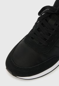 Sandalie atletice negre fabricate dintr-o combinație de materiale din suede și nylon. Prezintă o suprafață texturată, design cu șireturi și un accent alb al tălpii.