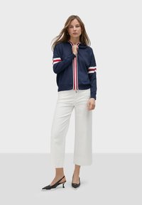 Marinblå zip-up hoodie med röda och vita ränder på ärmarna, matchad med vita vida byxor och svarta slingback-klackar.