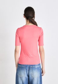 Camisa rosa coral texturizada de manga curta com decote redondo. A parte de trás apresenta um design liso e uma silhueta ajustada.