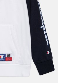 Felpa con cappuccio caratterizzata da un corpo bianco e maniche navy. Include una tasca frontale, logo ricamato e testo stampato lungo la manica.