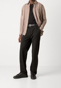 Jasnobrązowa lniana koszula, czarny bawełniany t-shirt, czarne spodnie i czarne sneakersy. Strój ma luźny krój i minimalistyczny design.