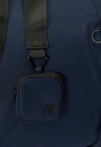 Mørkeblå ryggsekk med strukturert stoff, justerbar svart stropp og en liten glidelåslomme med svart metallhardware og logodetalj.