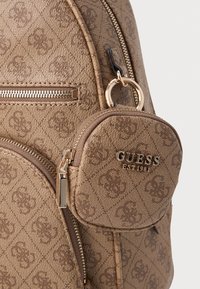 Zaino marrone con texture, dotato di una tasca con zip logata, hardware in tonalità oro e finitura decorata con design geometrici.