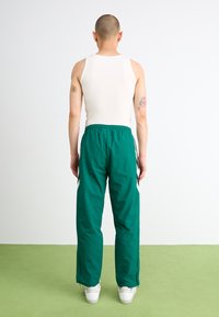 Groene trainingsbroek met een relaxte pasvorm, gemaakt van lichtgewicht stof. Heeft witte zijstrepen en ritsen aan de onderkant. Gecombineerd met een witte tanktop.