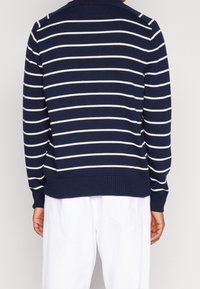 Pull-over en maille bleu marine avec des rayures horizontales blanches, poignets et ourlet côtelés, doté d'un col et d'une coupe décontractée.