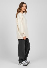 Felpa crema con spalle scese, abbinata a jeans neri larghi e sneakers grigie. Tessuto morbido, vestibilità rilassata, design minimal e colori neutri.
