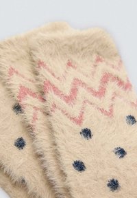 Calcetines beige difusos con un patrón en zigzag rosa y lunares azules. Textura suave con un acabado irregular y esponjoso. La vista en primer plano resalta el diseño.