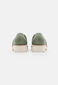 Chaussures en cuir vert avec un motif tissé texturé. Elles présentent une semelle en caoutchouc de couleur claire, un bout arrondi et un talon bas.