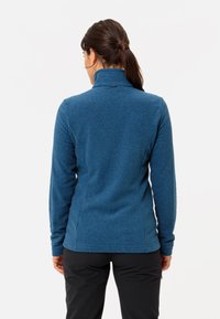 Pullover in pile blu con colletto alto, maniche lunghe e una texture liscia. Presenta un piccolo logo sul collo e un design aderente.