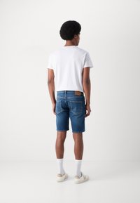 Shorts en denim bleu avec une coupe droite, cinq poches et une étiquette en cuir au dos. Associés à un t-shirt blanc uni et des chaussettes blanches.