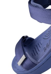 Siniset sandaalit, joissa on teksturoidut remmit ja pehmustettu pohja. Varustettu metallisella logo-aksentilla ja muotoillulla pohjalla mukavuutta varten.