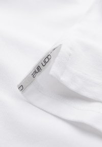 Gros plan d’un ourlet en tissu blanc avec une petite étiquette intérieure affichant un texte partiel noir « on line » cousue à l’intérieur de la couture.