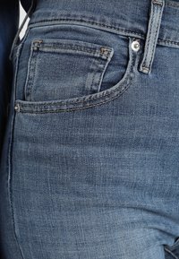 Blue denim jeans with a slightly faded wash, five-pocket design, finished waistband, and contrasting stitching.