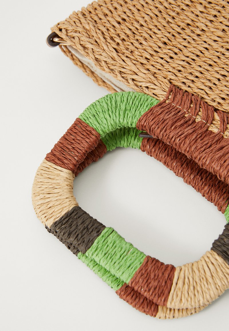 Bolso tote tejido con un cuerpo de paja natural y un asa trenzada multicolor en verde, marrón, negro y beige. La textura es áspera y orgánica.