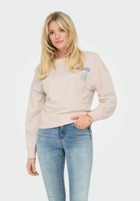 Sweatshirt rose clair à manches longues, avec des poignets côtelés et un ourlet arrondi. Présente un design graphique en texte bleu et orange sur le devant.
