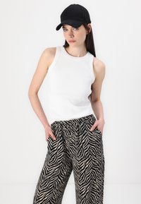 Bjela rebrasta majica bez rukava uparena s hlačama širokog kroja sa zebrastim uzorkom u crnoj i krem boji. Crna bejzbol kapa upotpunjuje odjevnu kombinaciju.