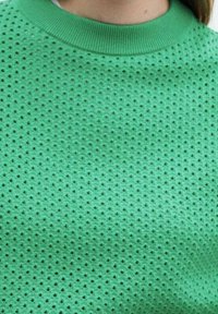 Groene geperforeerde gebreide trui met een ronde ribbelkraag. De textuur heeft kleine gaten die gelijkmatig over de stof verdeeld zijn.