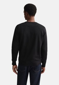 Schwarzer Pullover mit Rundhalsausschnitt, gerippten Bündchen und Saum. Glatte Textur, Rückendetails sichtbar, getragen über dunkelblauen Jeans.