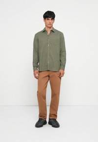 Groen geruit overhemd met lange mouwen, relaxed fit, geknoopt, gecombineerd met lichtbruine rechte broek en zwarte sneakers.