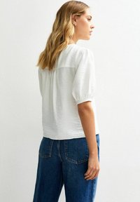 Witte textuurblouse met pofmouwen, gecombineerd met high-waisted blauwe spijkerbroek. Eenvoudig ontwerp met een stijlvolle achterkant.