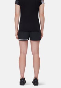 Svart träningsöverdel med korta ärmar, svarta shorts med en vit rand, och svarta träningsskor. Synlig tygstruktur och passform.